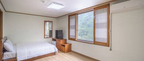 Une chambre à coucher avec un lit, une télévision, une petite table en bois et une fenêtre donnant sur un paysage verdoyant.