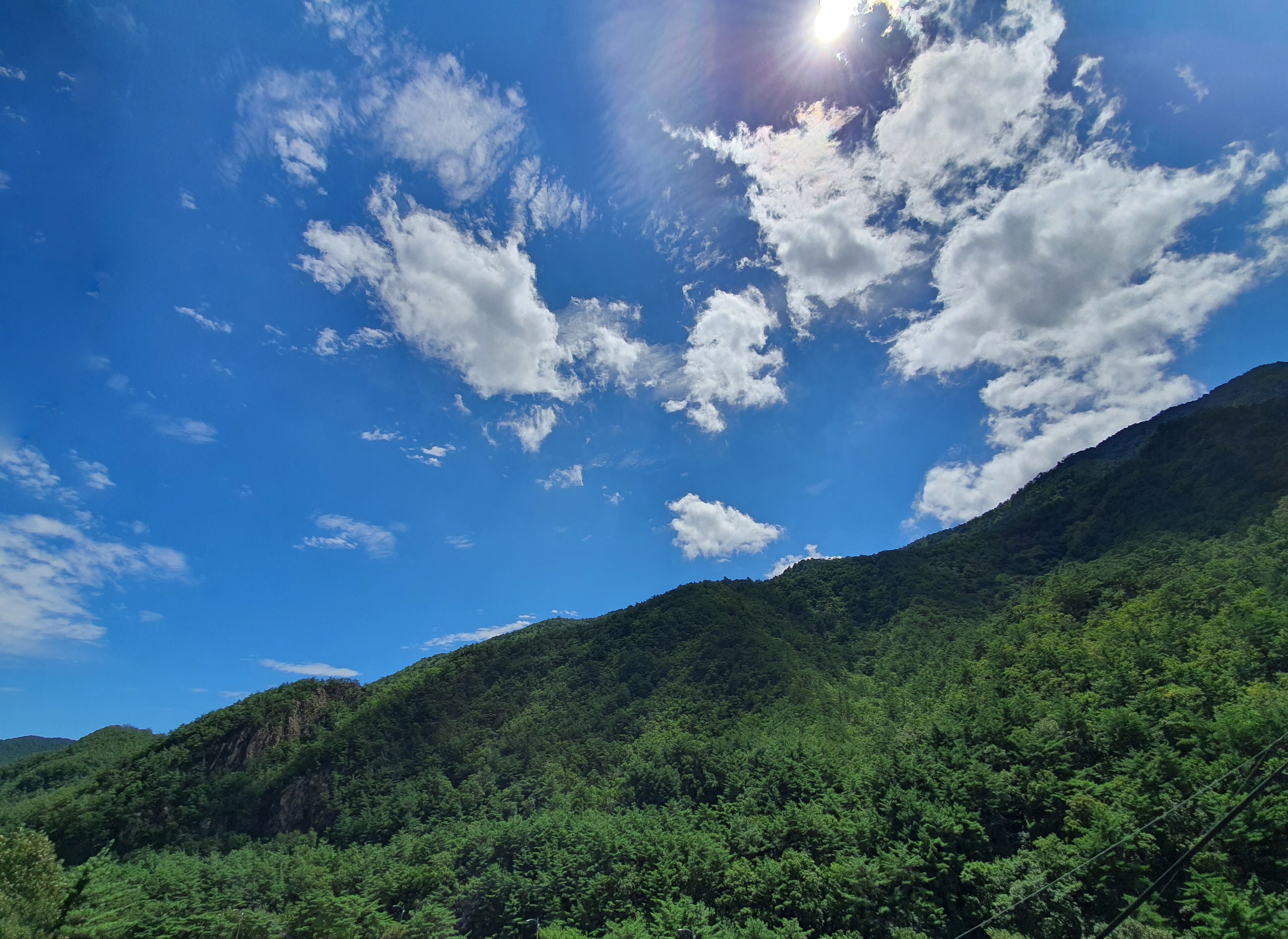 Un paisaje montañoso con densos bosques verdes y un cielo azul despejado con nubes dispersas.