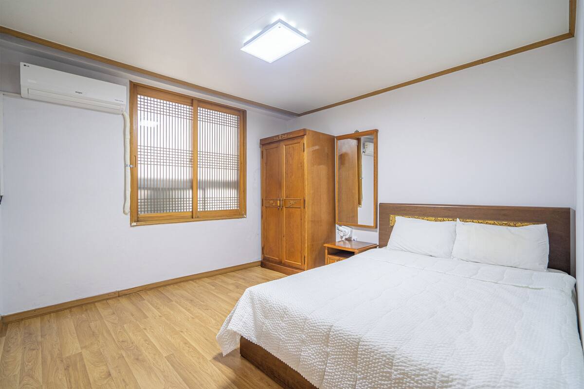 Ein Schlafzimmer mit Bett, Holzschrank und einem Fenster mit Jalousien.