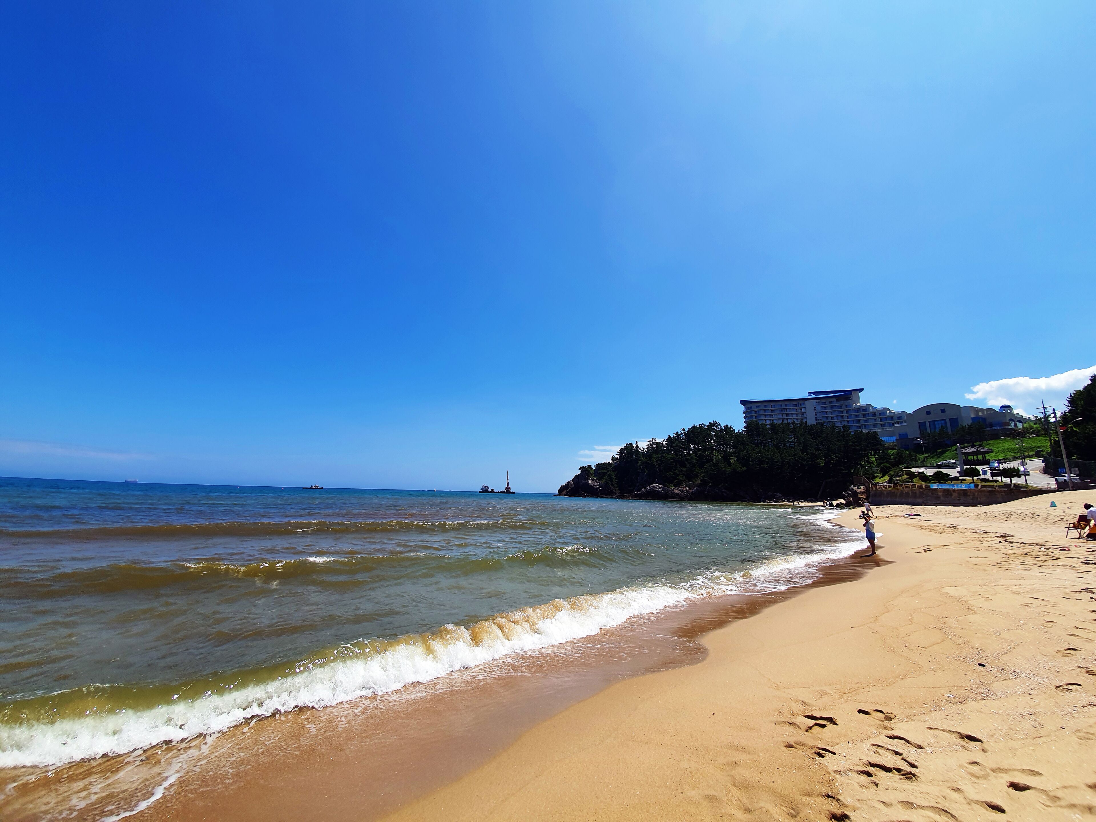 A beach with a clear sky, a sandy shore, and a building in the background.