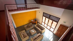 A spacious living area with multiple sofas and a coffee table, a small side table with a lamp, and a large window with a wooden door.