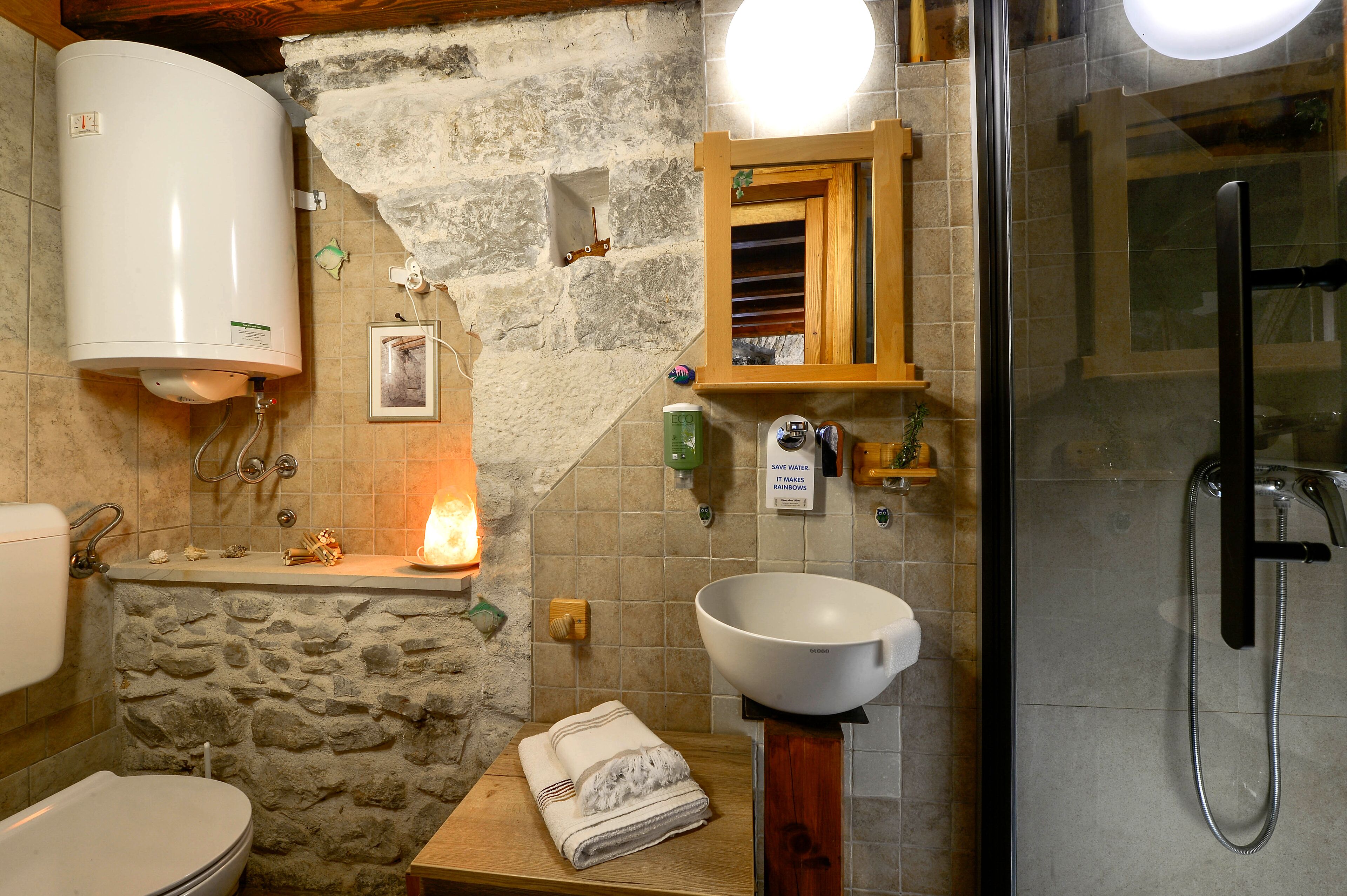 Un baño con pared de piedra, lavamanos blanco, ducha y tocador de madera.