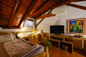 Ein gemütliches Zimmer mit Holzbalkendecke, einem Bett, einem Fernseher, einem Gemälde und einem kleinen Tisch mit Lampe.