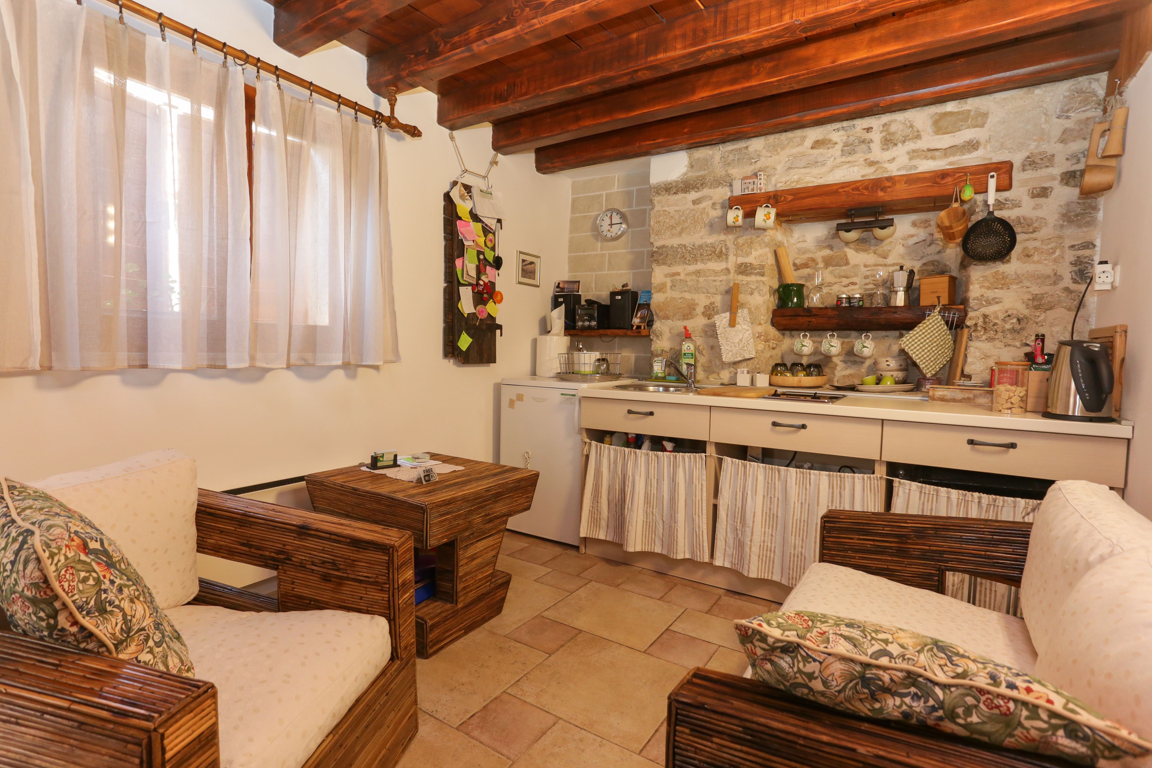 A cozy living room with wooden furniture, a kitchen with stone walls, and a rustic ceiling.