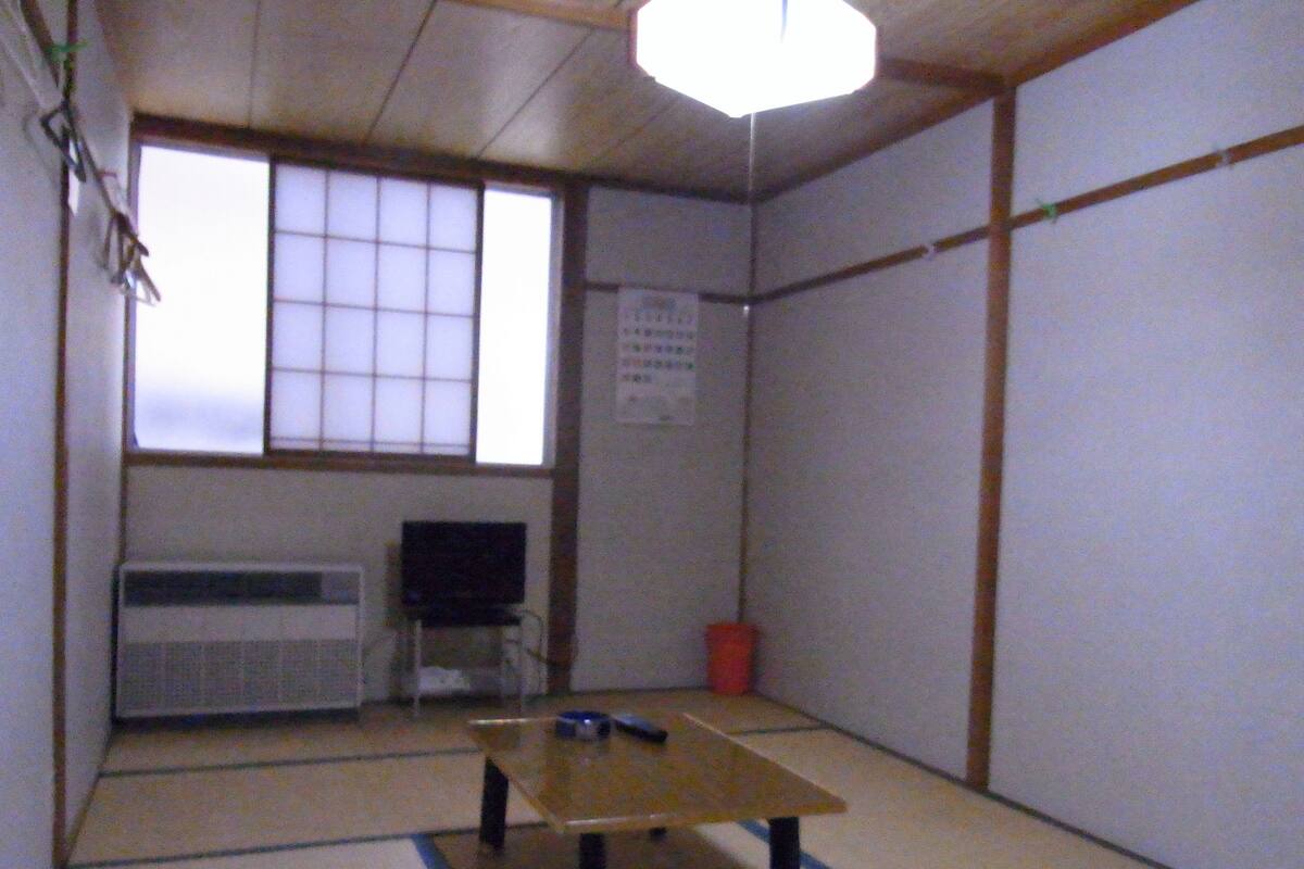 Perinteinen japanilainen huone, jossa on tatamimatto, matala pöytä, televisio ja ikkuna, jossa on shoji-paperi-ikkunaluukut.