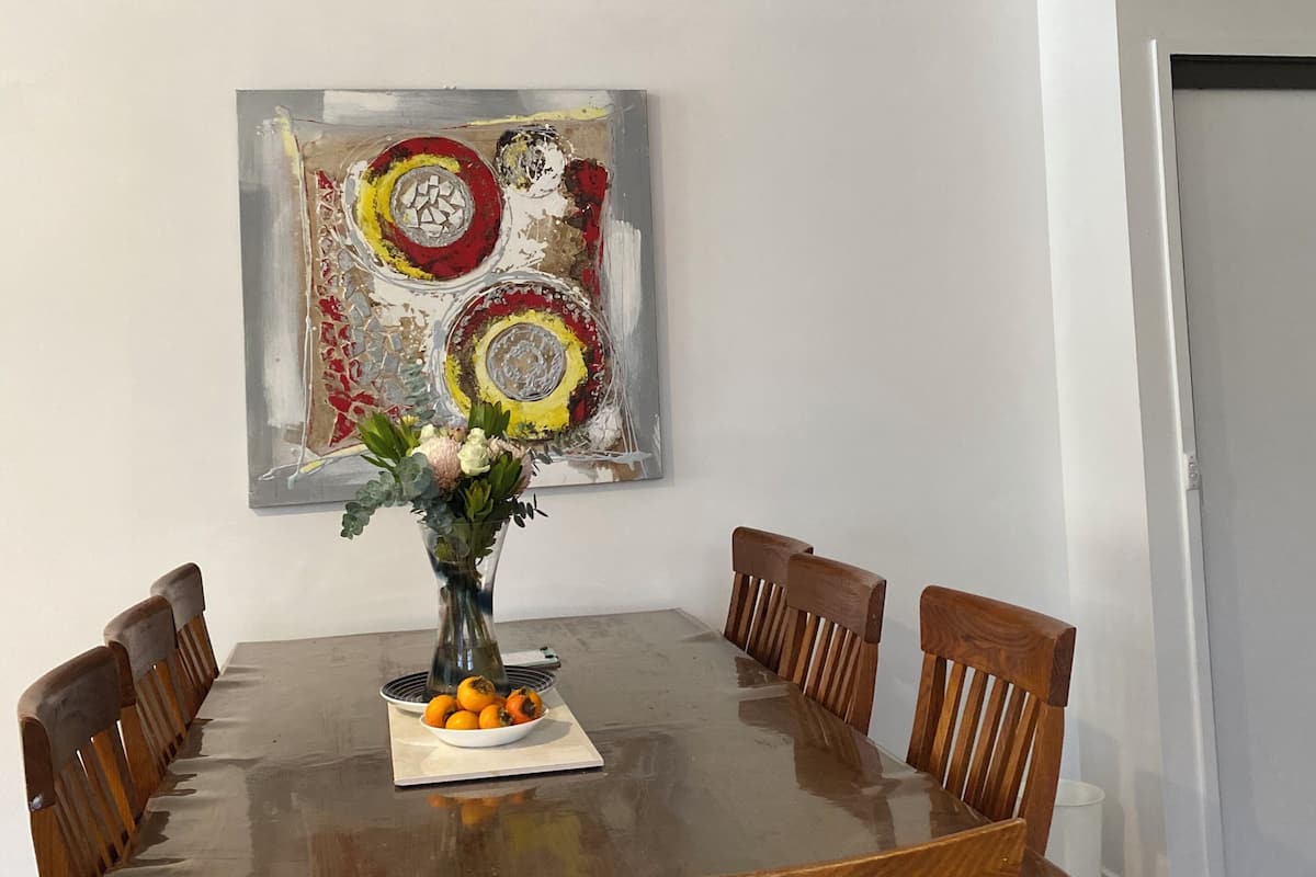 A dining room with a wooden table, six chairs, a ceiling fan, and a decorative painting on the wall.