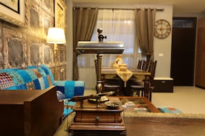 A vintage typewriter on a wooden table in a living room with a patterned blue sofa, a lamp, and a dining area in the background.