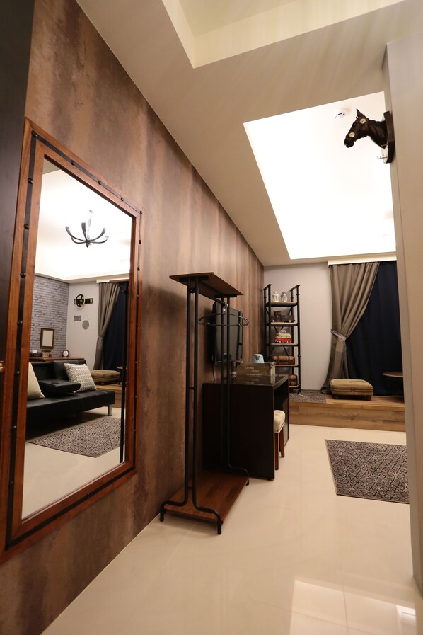 A modern living room with a large mirror, a ceiling light, a bookshelf, and a small table.