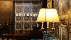 Una habitación con una lámpara antigua, un sofá con una manta estampada y una pared con el texto "ARIA HOME".