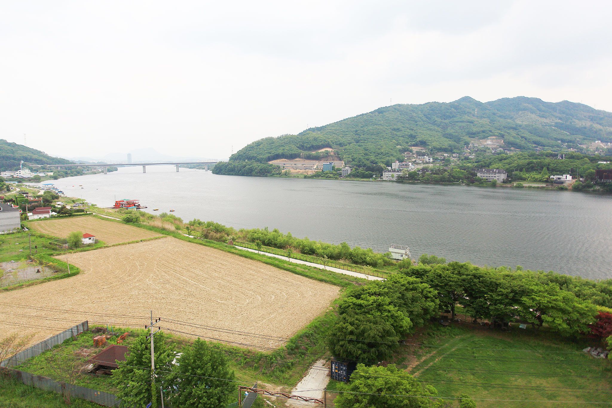 A river with a bridge, green hills, and a field with a fence.