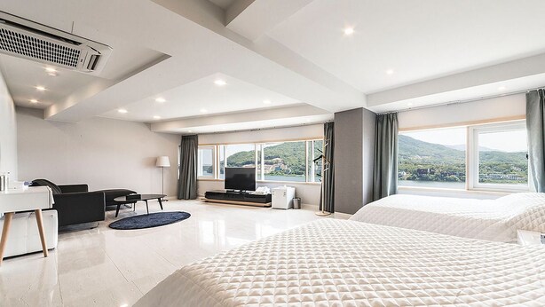 A modern hotel room with two beds, a desk, a chair, a TV, and large windows with a view of greenery. - J hotel (Yangpyeong)