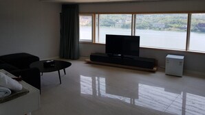 A modern living room with a large window, a flat-screen TV, a sofa, a coffee table, and a small cabinet. - J hotel (Yangpyeong)