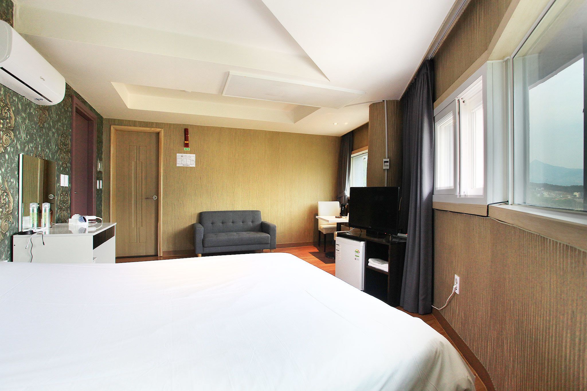 A hotel room with a large bed, a desk with a computer, a chair, a television, and a window with a view.