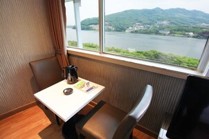 Habitación de hotel con vistas a un río y colinas, una mesa con una tetera y un menú, y una silla.