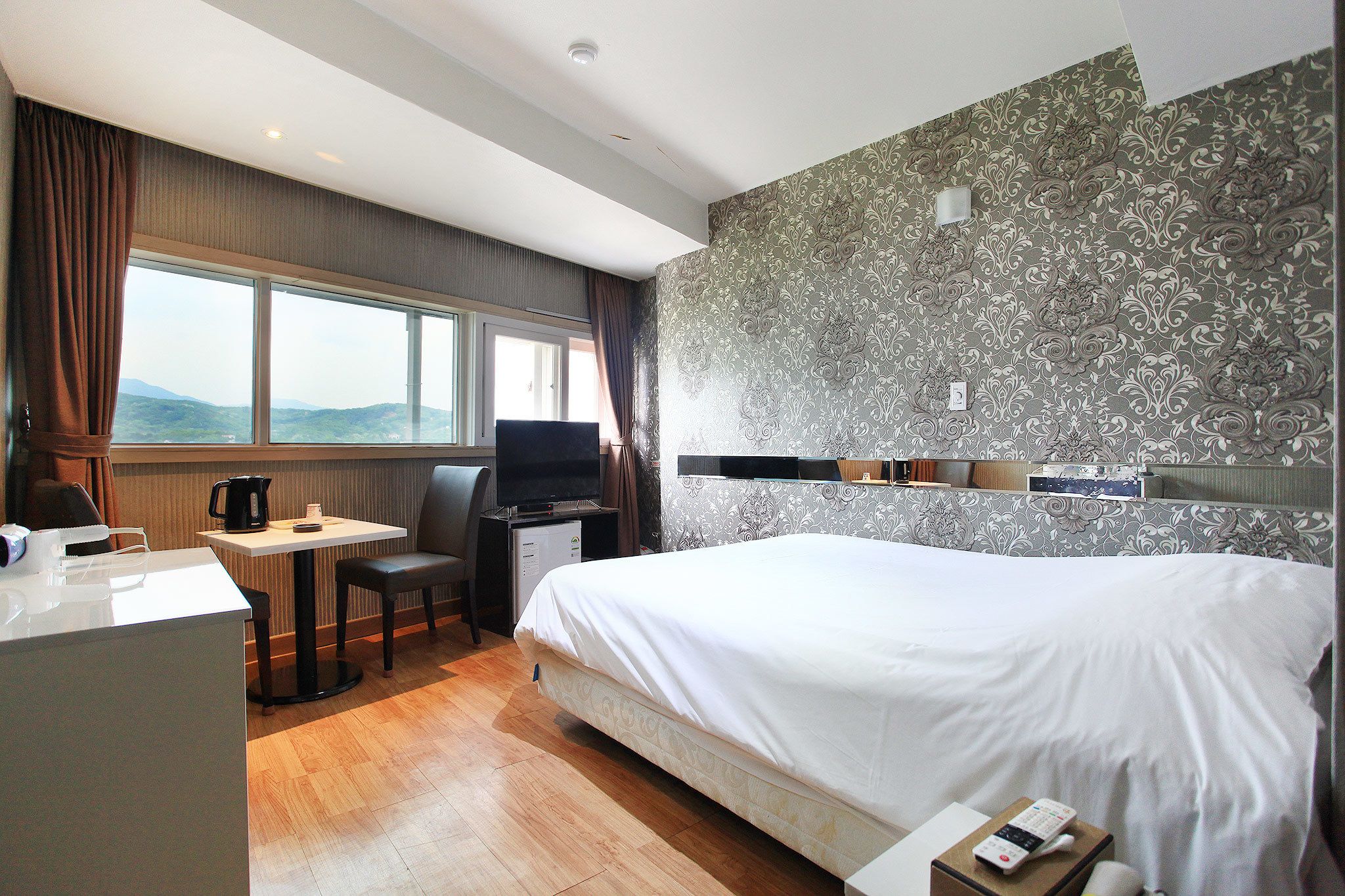 Habitación de hotel con una cama grande, un escritorio con silla, televisión y ventana con cortinas.