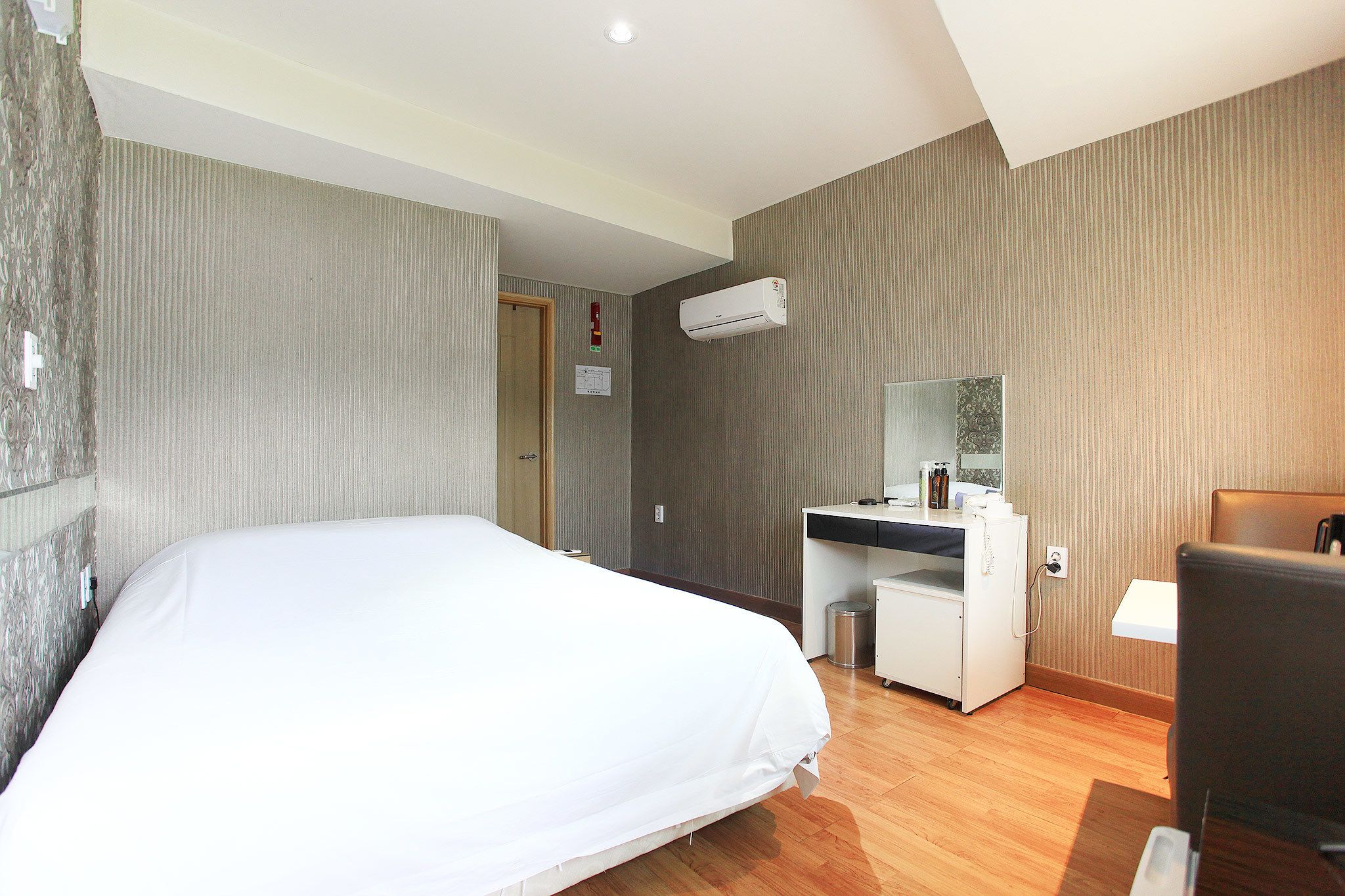 A hotel room with a bed, a desk, a chair, and an air conditioning unit.