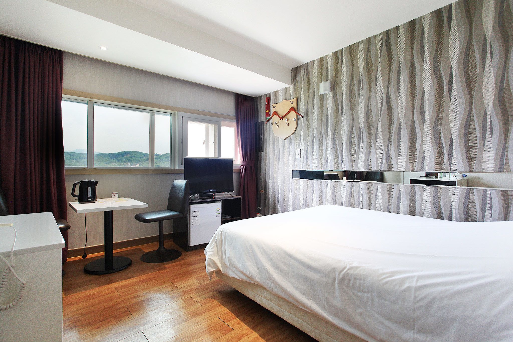 A hotel room with a bed, a desk with a computer, a television, and a window with a view of the hills.