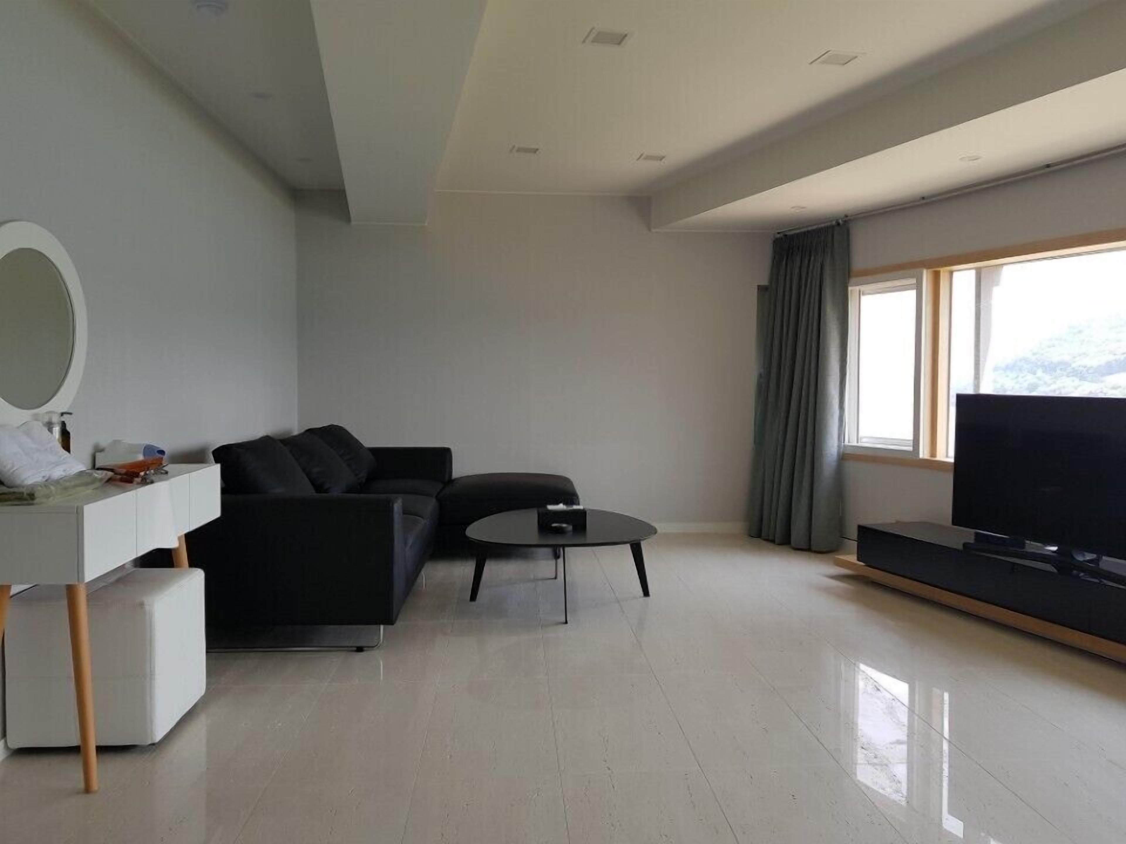 A modern living room with a black sofa, a small coffee table, a flat-screen TV, and a large window with curtains.