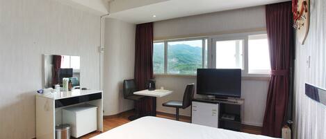 Habitación de hotel con cama, escritorio, televisor y ventana con vistas a las montañas.