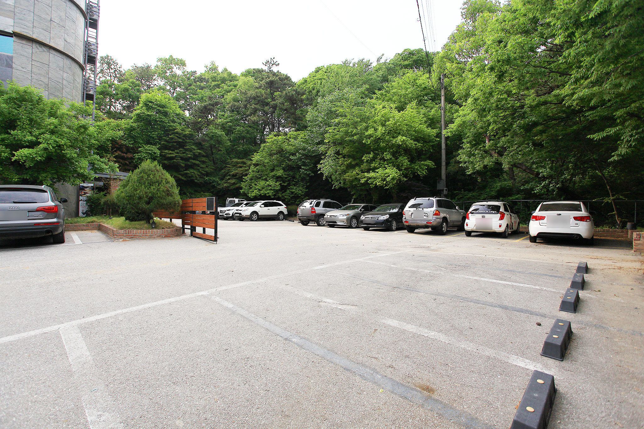 A parking lot with several cars parked, surrounded by trees and a building.