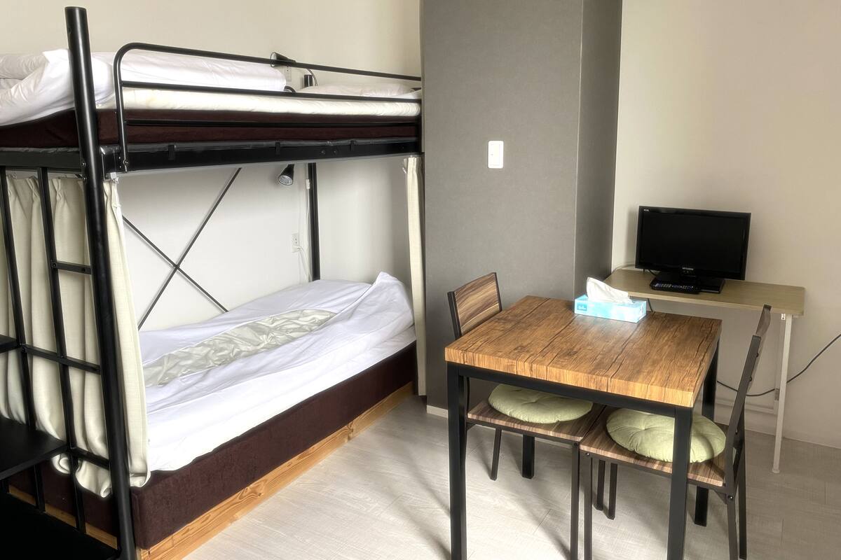 A bunk bed with a desk and chair, a television, and a window.