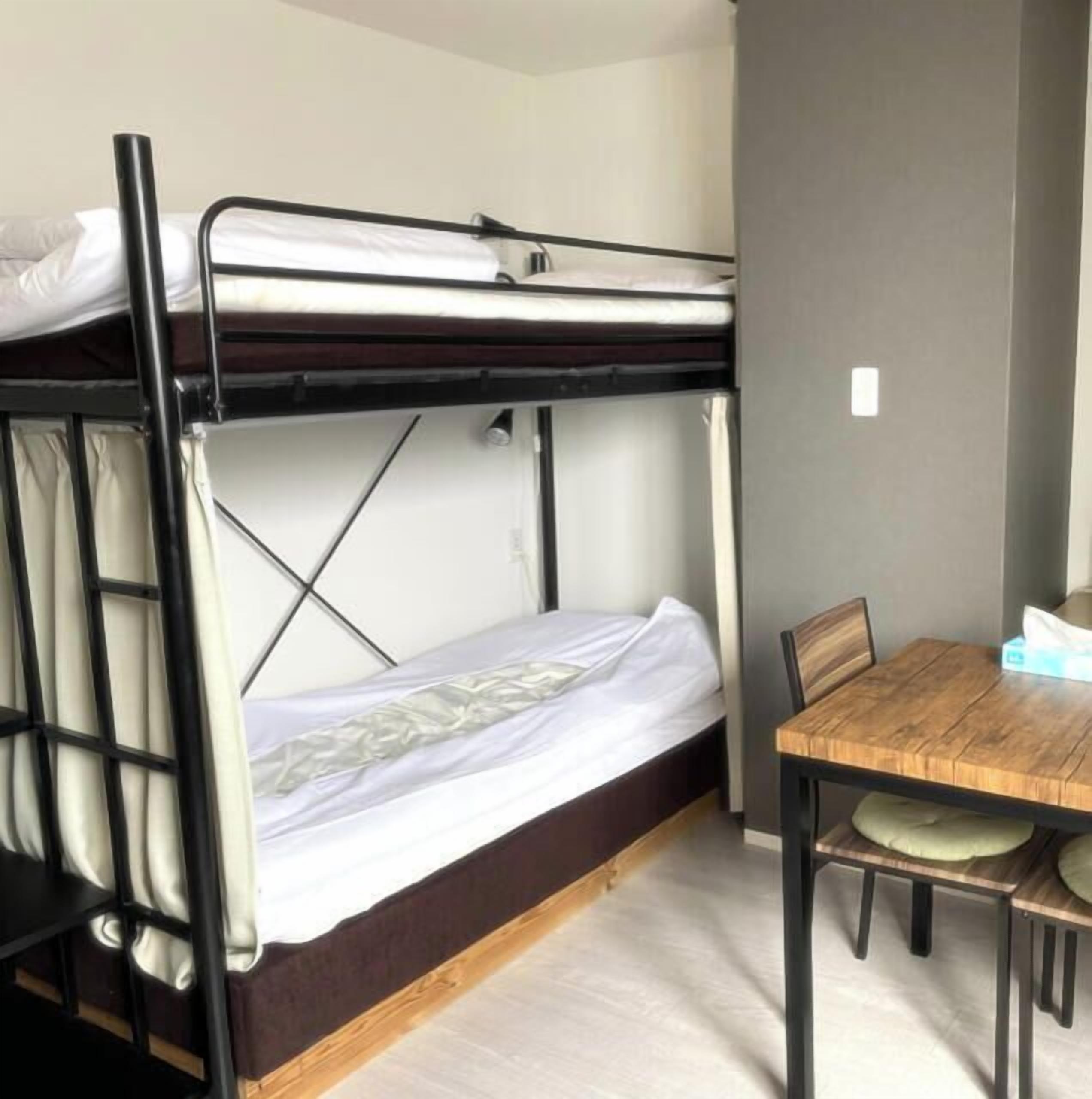 Ein Etagenbett mit Holztisch und Stühlen, eine weiße Wand und ein heller Boden.