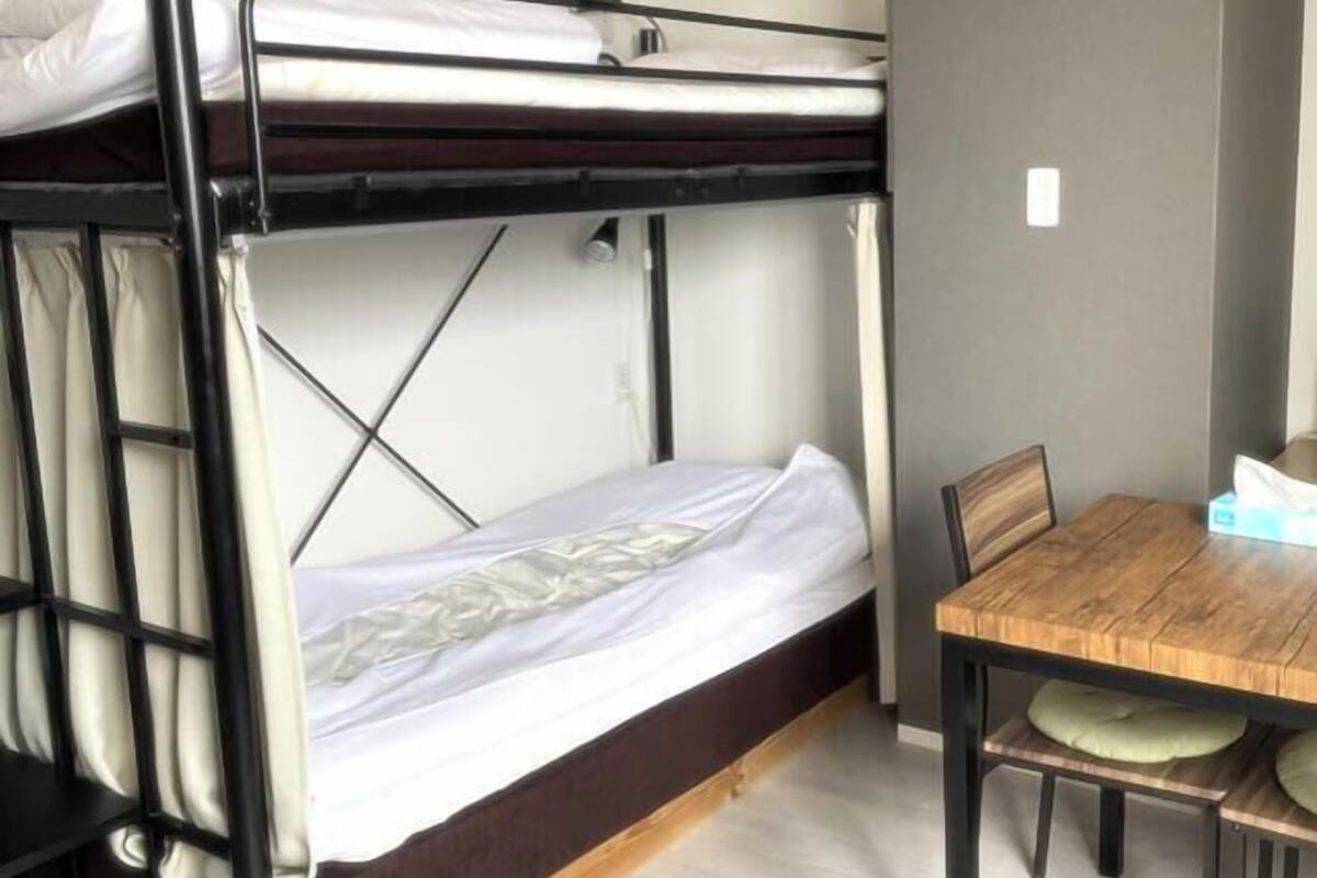 A bunk bed with a wooden table and chairs, a white wall, and a light-colored floor.