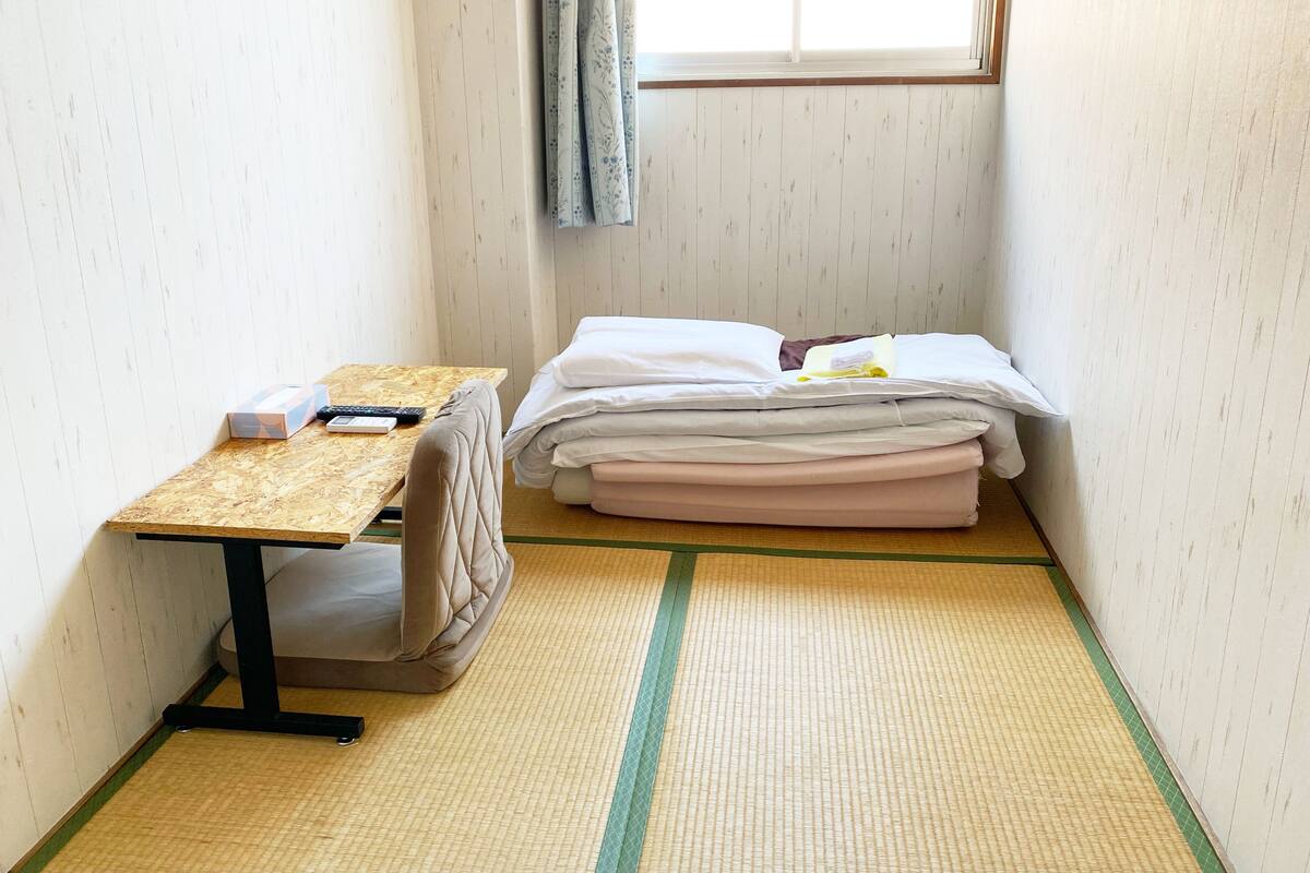 A small room with a bed, a table, and a window.