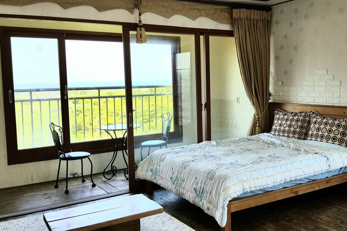 Ein Schlafzimmer mit Bett, Stuhl, Tisch und einem Balkon mit Blick.