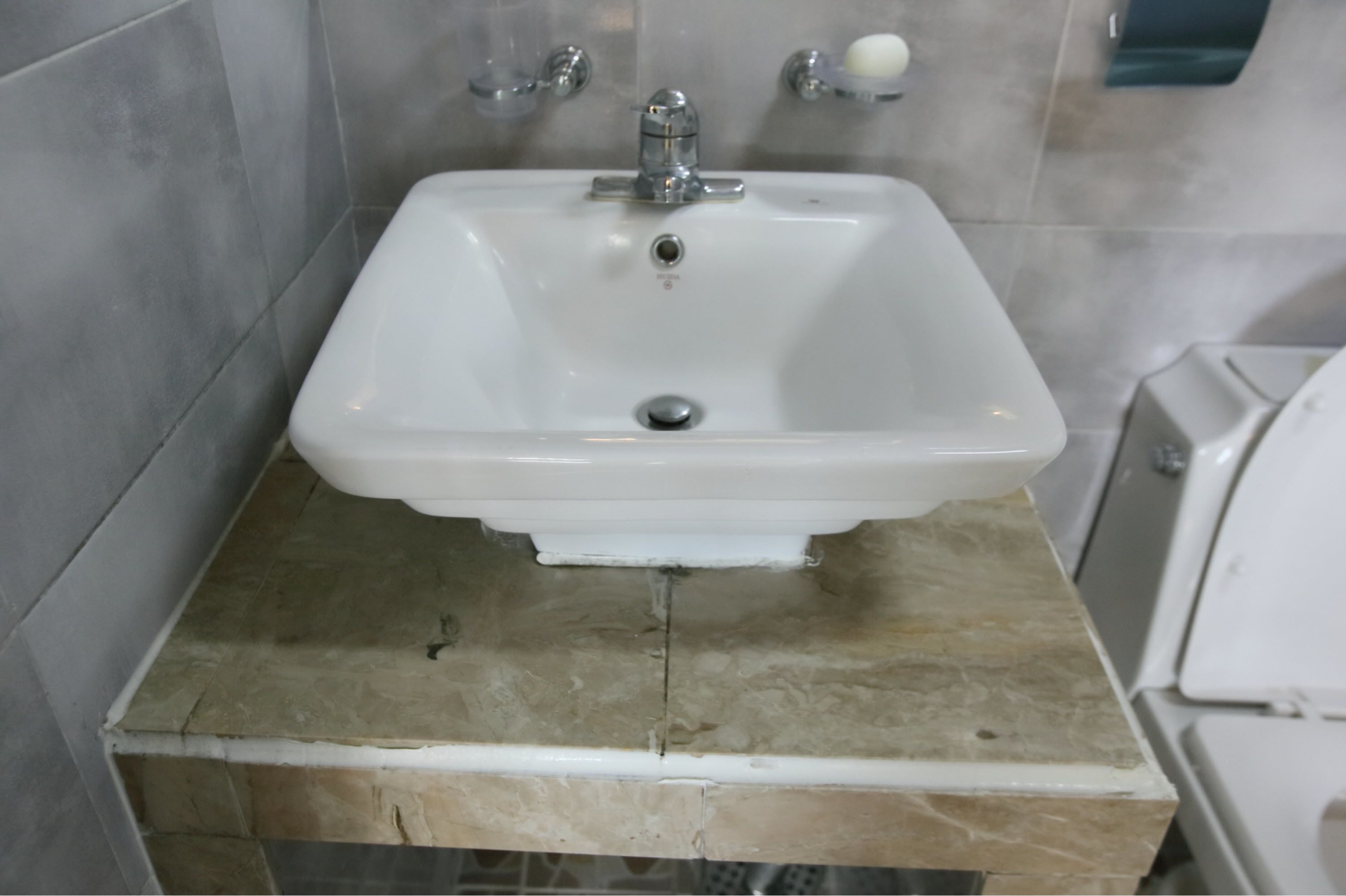 Un baño con un lavamanos blanco, un espejo y un jabonera en la pared.