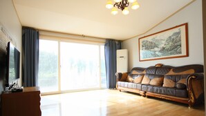 A spacious living room with a large sofa, a flat-screen TV, and a sliding glass door leading to a balcony. - Blaze Resort Jeju (Seogwipo)