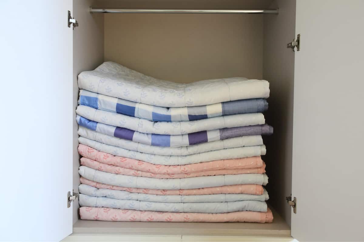 A closet with neatly stacked bedding in various colors.