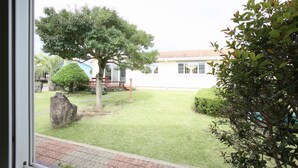 A view of a well-maintained lawn with a large tree, a stone, and a building in the background. - Blaze Resort Jeju (Seogwipo)