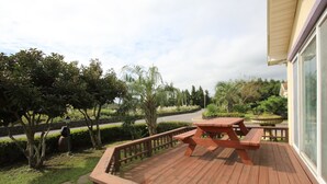 A wooden deck with a picnic table, surrounded by greenery and a view of a road. - Blaze Resort Jeju (Seogwipo)