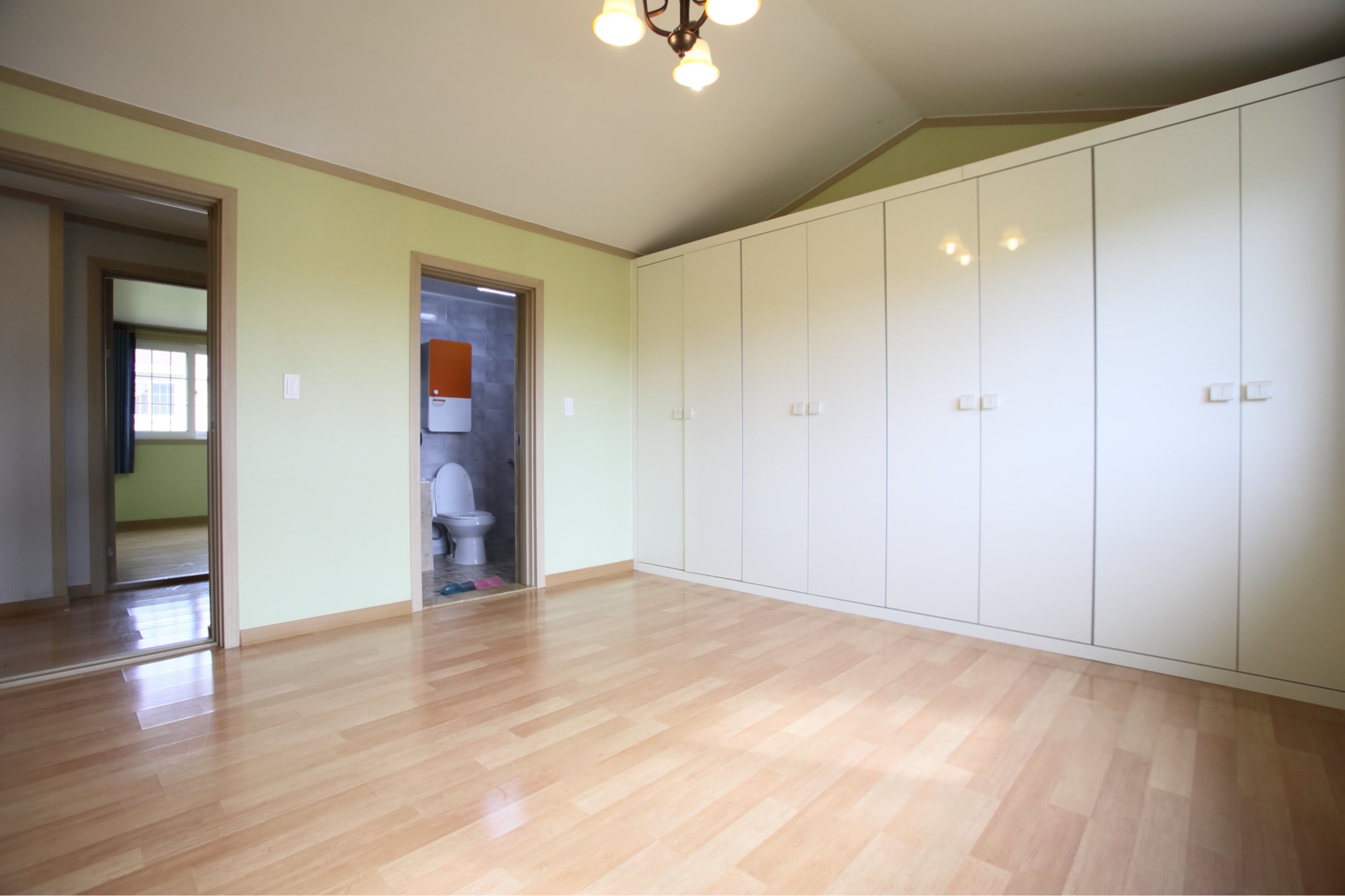 Une pièce spacieuse avec un plancher en bois, une grande armoire et une porte donnant sur une salle de bain.