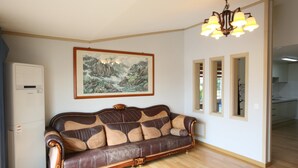 A living room with a brown leather sofa, a framed painting on the wall, and a chandelier. - Blaze Resort Jeju (Seogwipo)