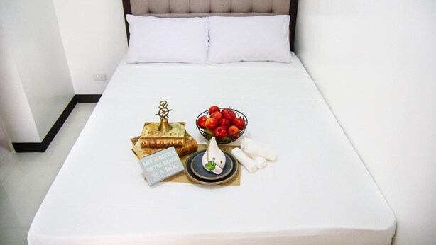 Una cama bien hecha con edredón blanco, cabecera y un frutero pequeño sobre la cama.