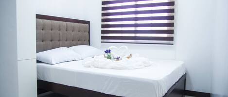 Una cama bien hecha con sábanas blancas y un arreglo decorativo de flores y un pequeño jarrón.