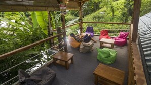 An outdoor seating area with wooden tables and colorful bean bags, surrounded by lush greenery. - Dorme Tree (Labuan Bajo)