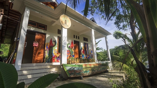 A white building with a porch, a sign reading "DORMETREE," and colorful artwork on the windows. - Dorme Tree (Labuan Bajo)