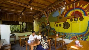 A restaurant with wooden tables and chairs, a mural on the wall, and a view of the outdoors through a window. - Dorme Tree (Labuan Bajo)