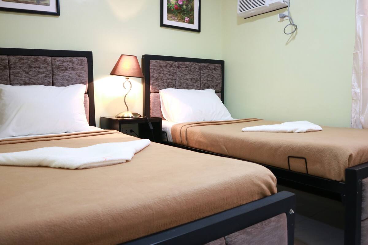 Two twin beds with brown bedding, a bedside lamp, and a wall-mounted air conditioner.