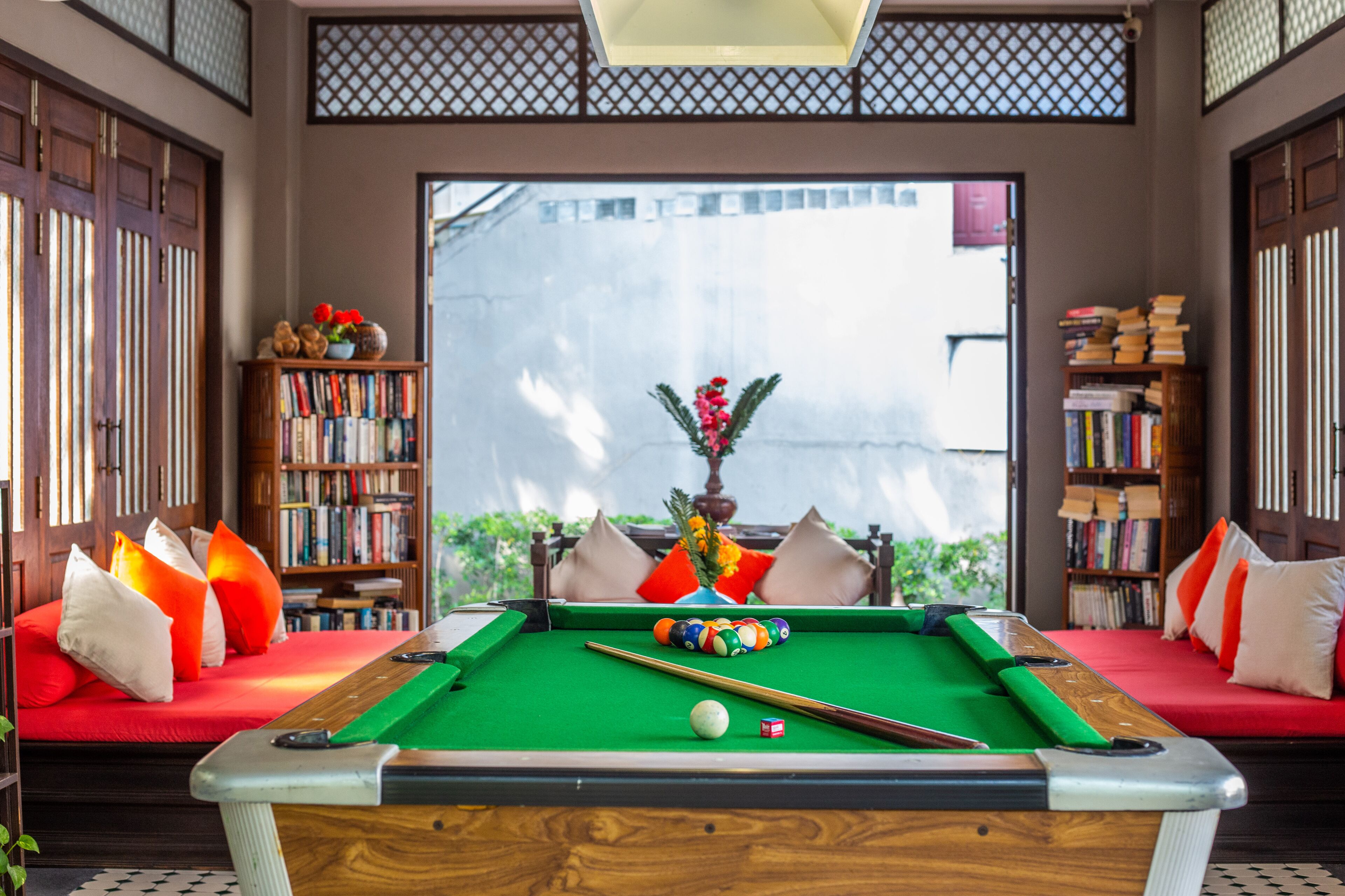 Een pooltafel in een kamer met een bank, boekenkasten en uitzicht door een raam.