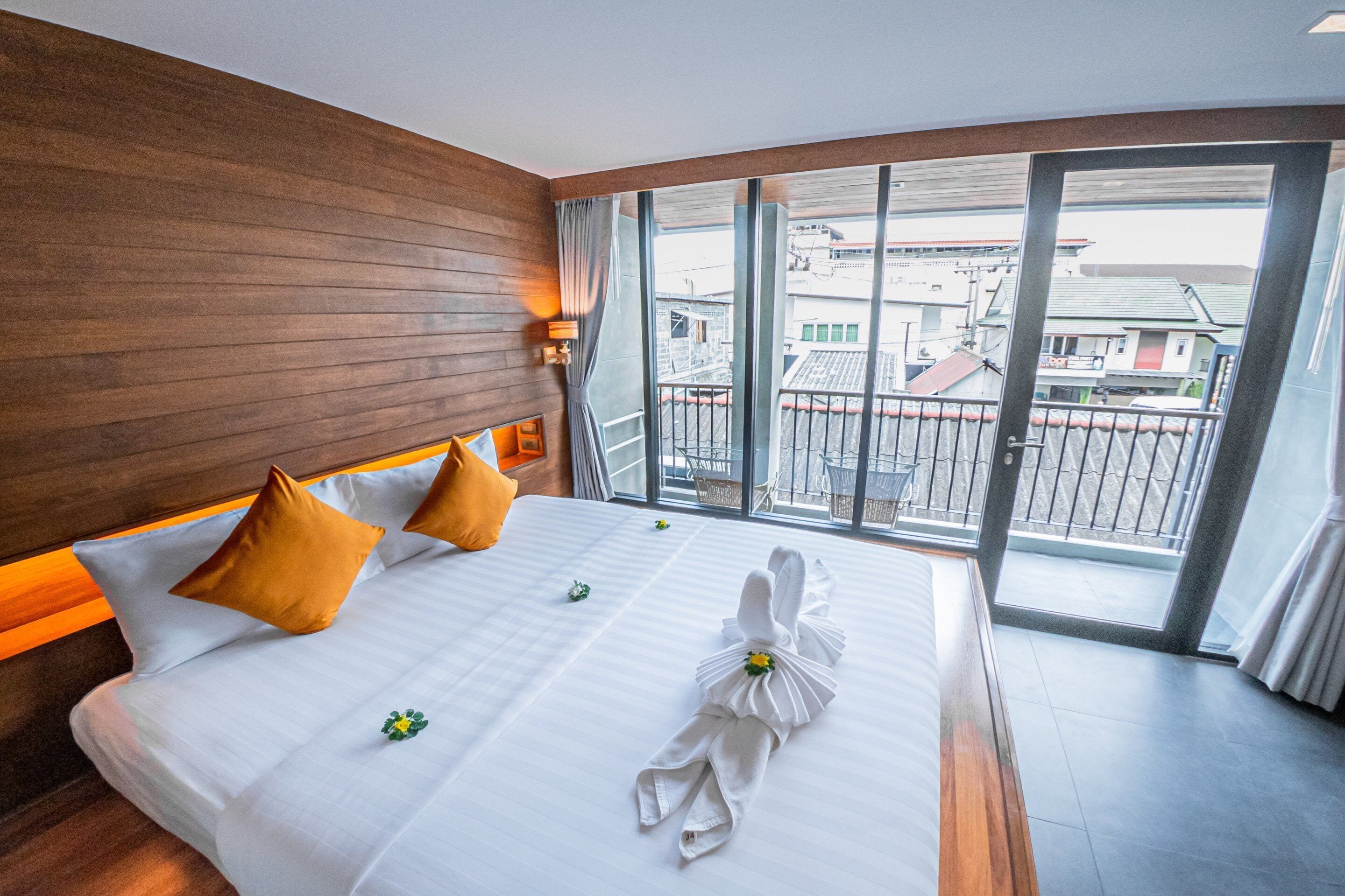 Een hotelkamer met een groot bed, een houten hoofdeinde en uitzicht op gebouwen door grote ramen.
