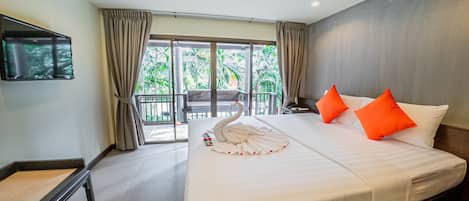 Habitación de hotel con una cama grande, un televisor montado en la pared, un balcón con vistas a palmeras y un área de comedor con mesa y sillas.