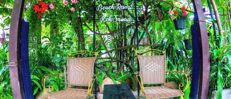 Un jardín con dos sillas de mimbre y una mesa bajo una pérgola, con un cartel que dice "Chuweng Garden Beach Resort".