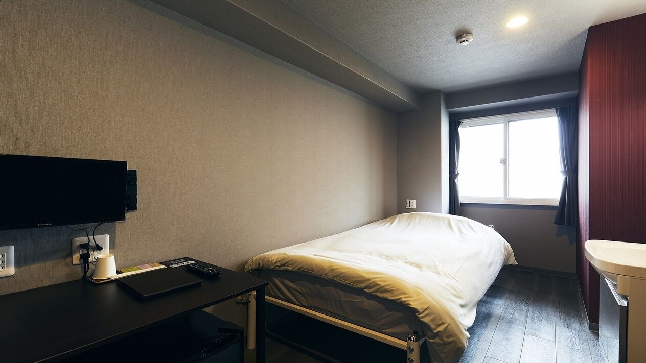 A hotel room with a bed, a desk with a computer, a television, a window with curtains, and a bathroom.