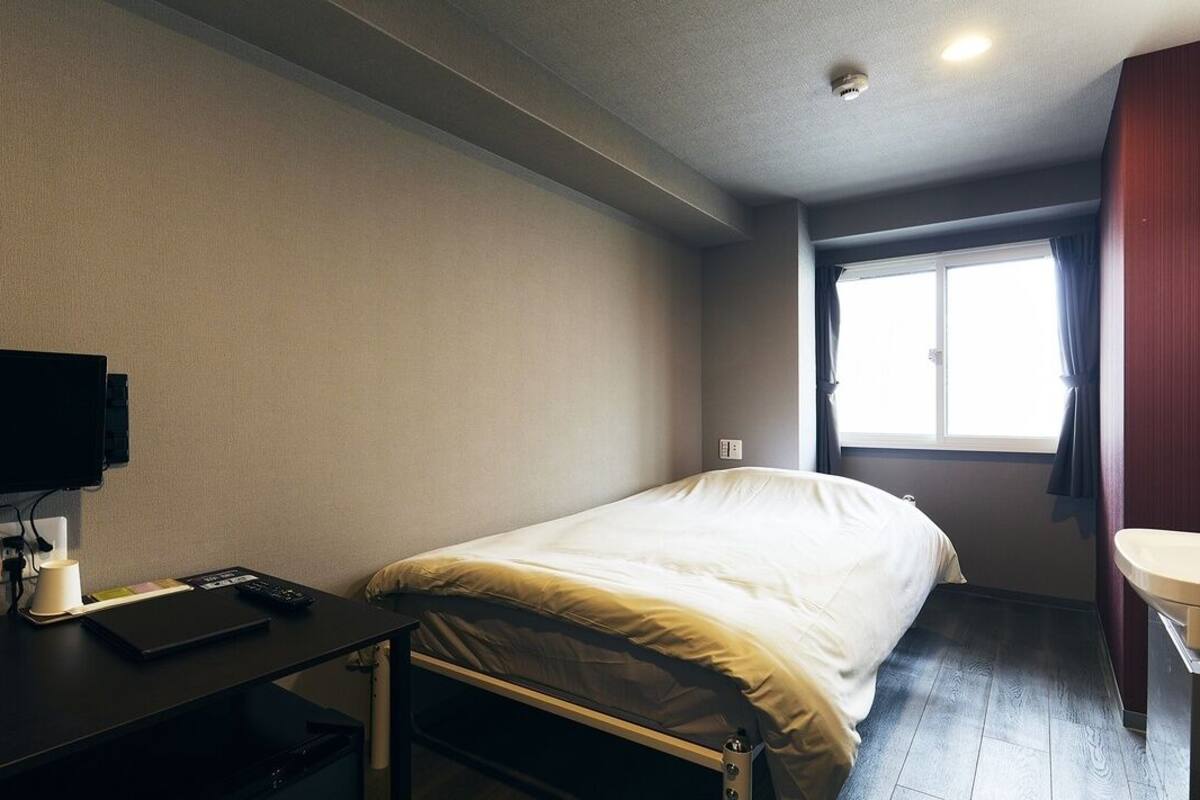 Una habitación de hotel con cama, escritorio con computadora, televisión, ventana con cortinas y baño.