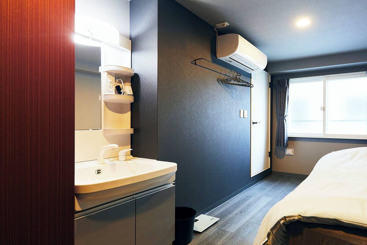 Una habitación de hotel moderna con cama, baño con lavamanos y espejo, y ventana con cortinas.