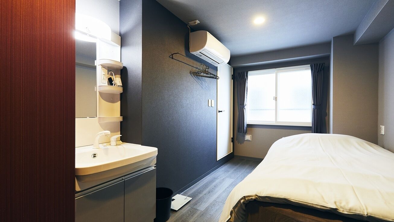 A hotel room with a bed, a window with curtains, a sink, and an air conditioning unit.